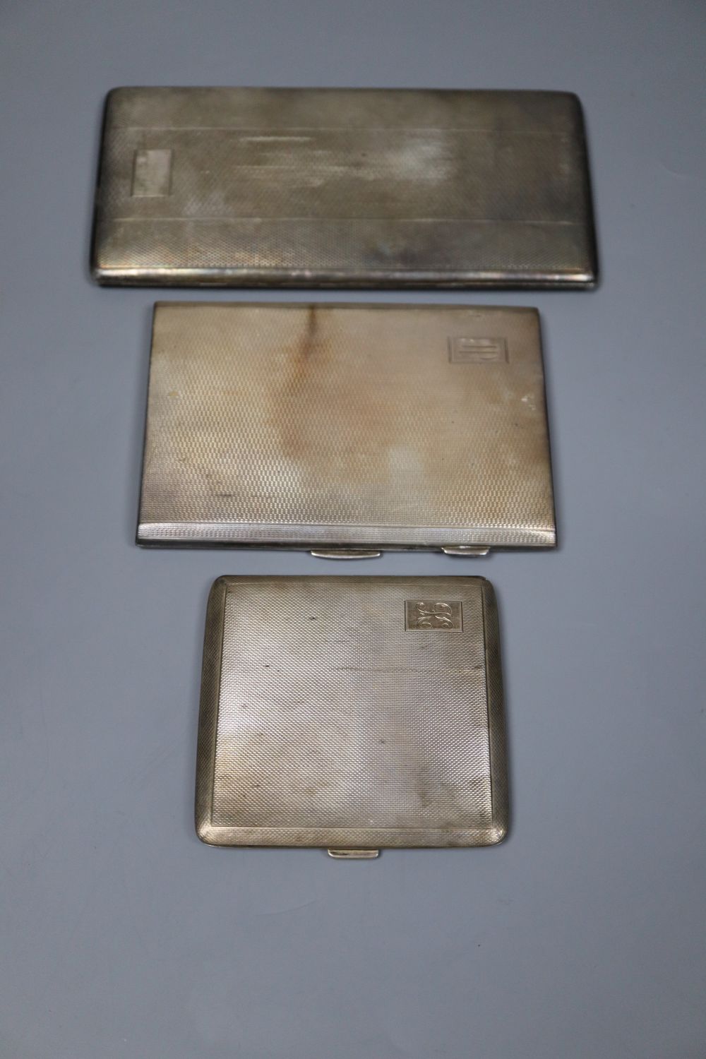 Three assorted mid 20th century silver engine turned cigarette cases, largest 16.8cm, gross 18oz.
